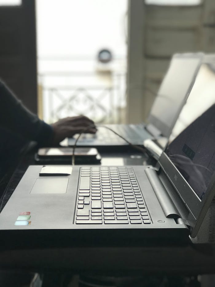 A backlit image of a person typing on laptops at a table, showcasing technology in use.