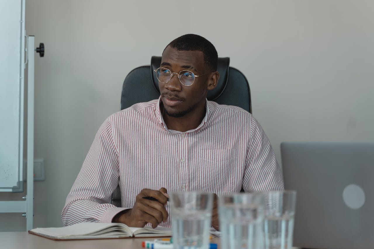 African American man in a striped shirt sits at a desk in an office environment.