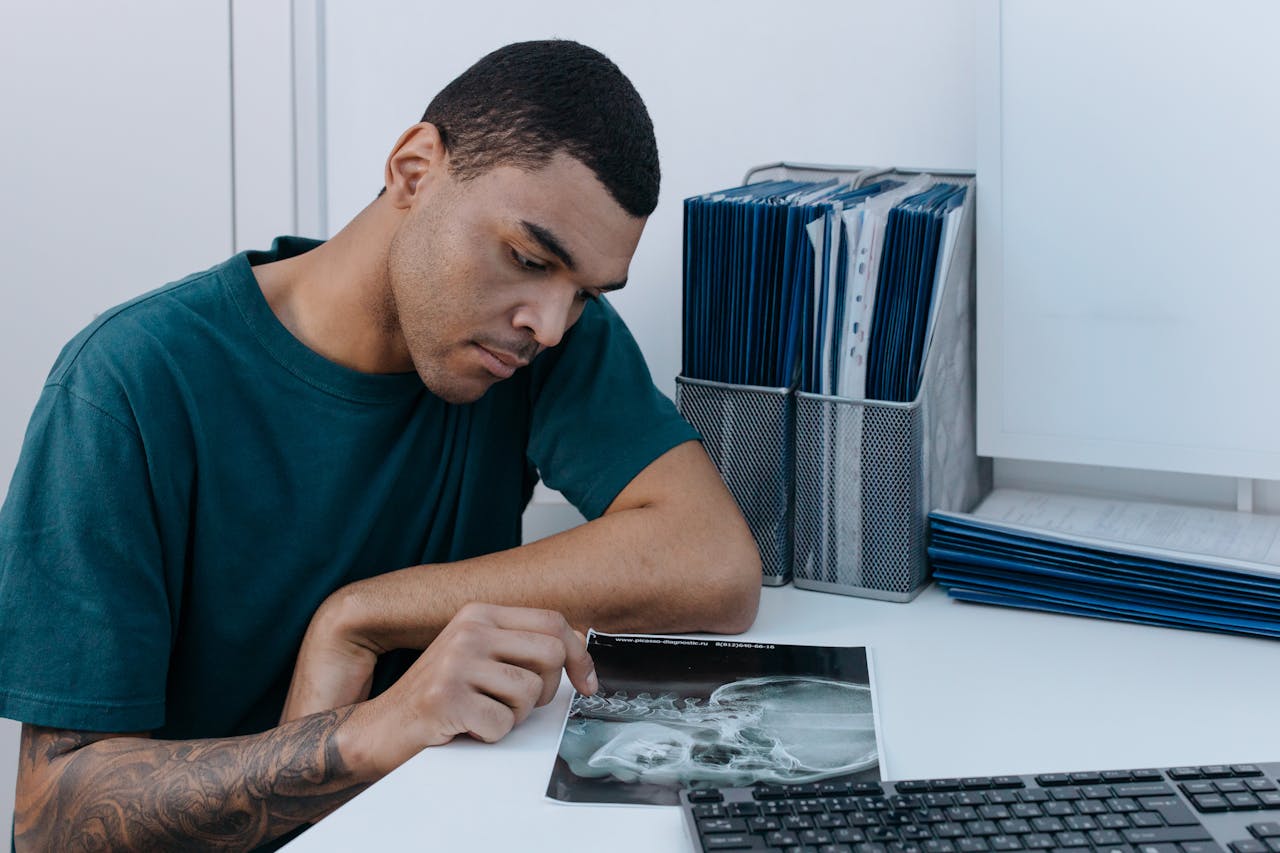 A man examines a dental X-ray at a clinic table, focusing intently on the image.