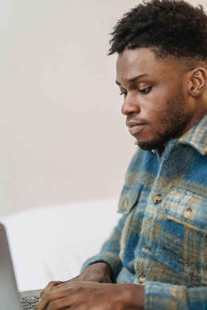 Young man in casual attire focusing intently while working on a laptop indoors.